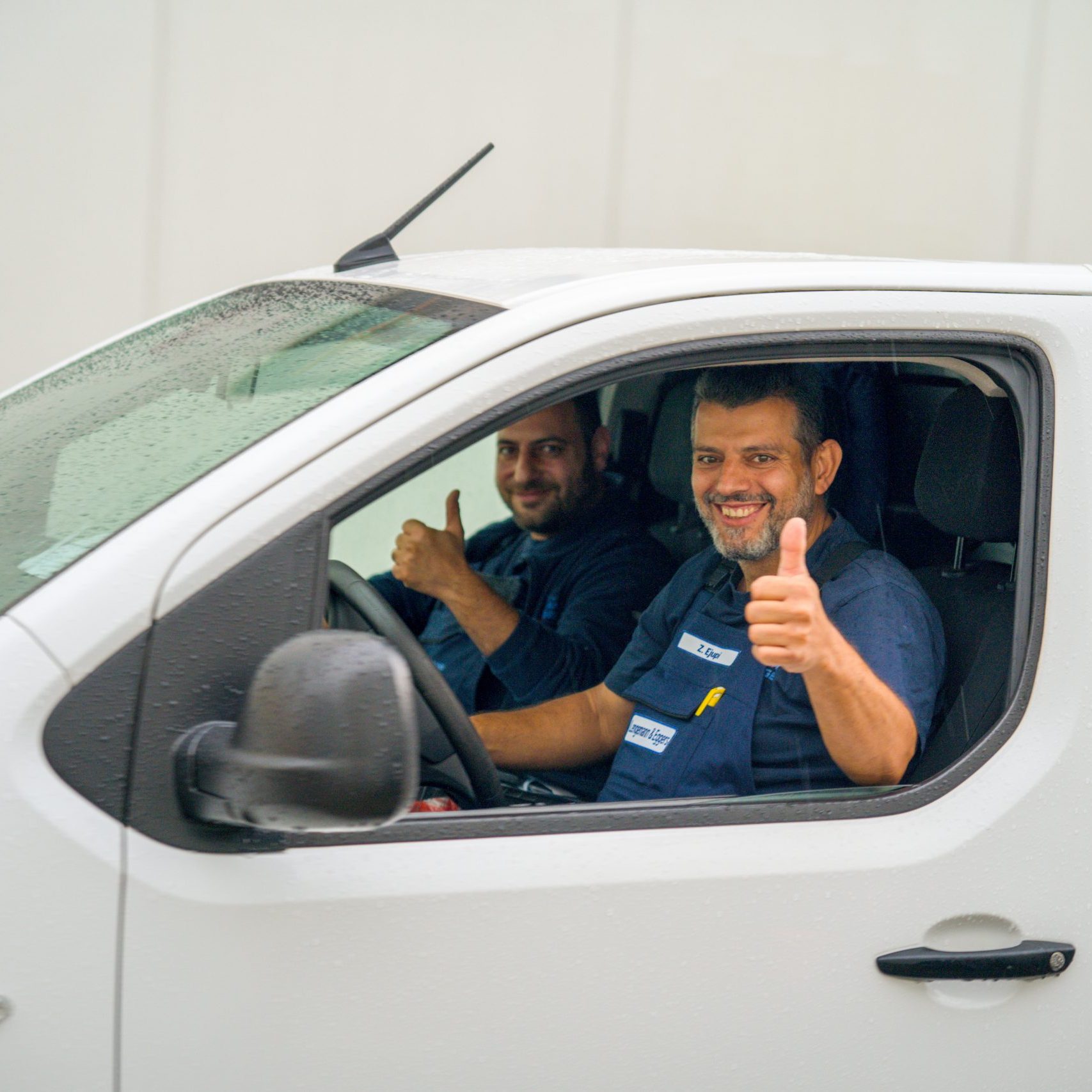 Zwei Handwerker sitzen im Auto und geben fröhlich ein Daumen hoch