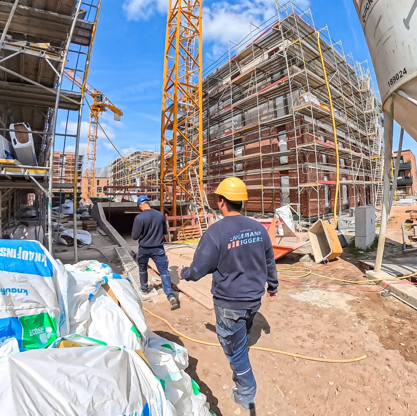 Zwei Handwerker mit Helm auf dem Kopf laufen über eine Grossbaustelle